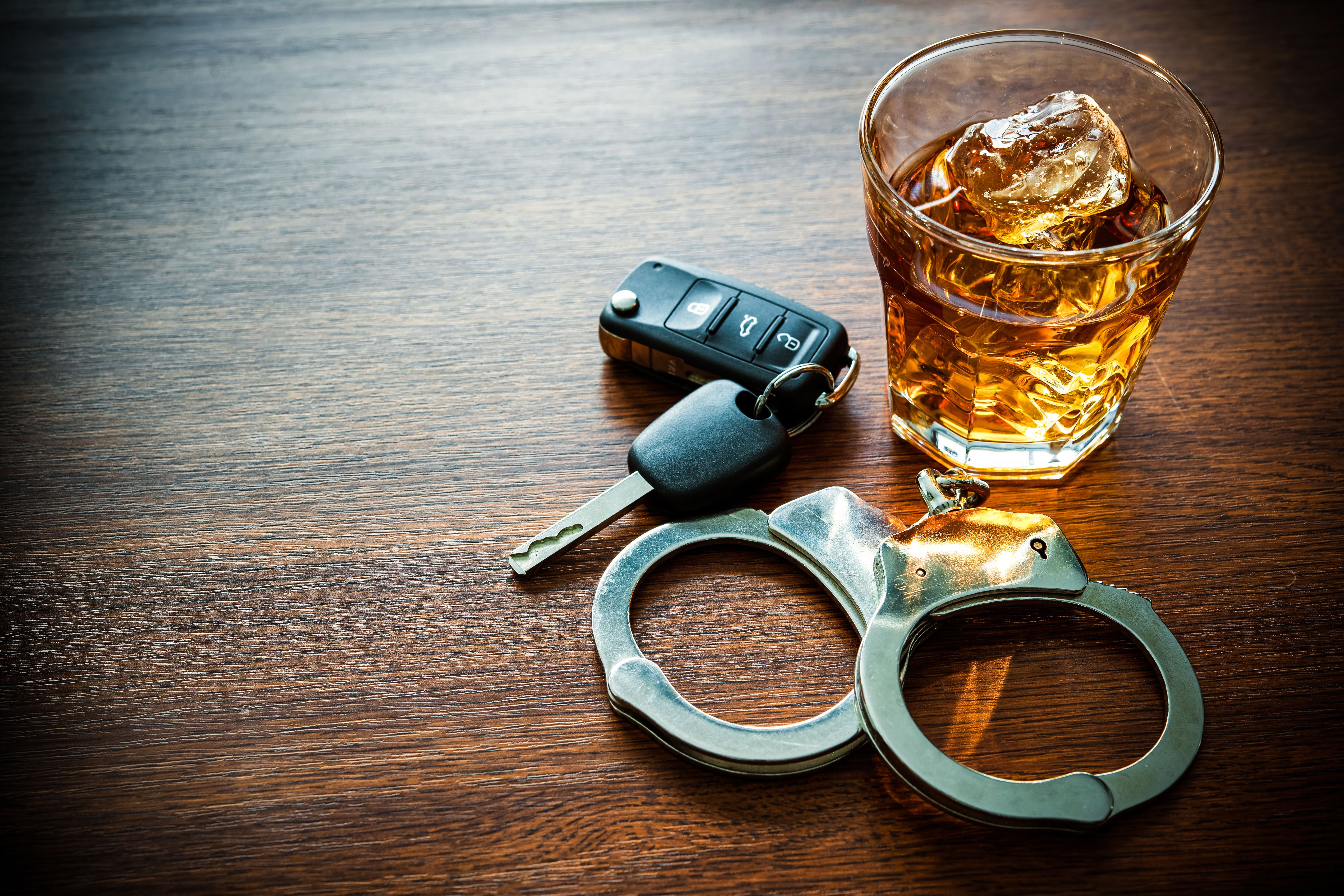 A sobering image of a glass of whiskey, car keys, and handcuffs on a wooden surface, representing impaired driving consequences.